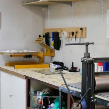 Einblick in unsere Druckwerkstatt, Siebdruckmaschine auf einer Arbeitsfläche, daneben eine Druckpresse.