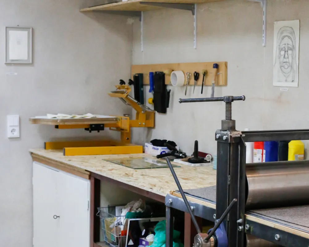 Einblick in unsere Druckwerkstatt Einblick in unsere Druckwerkstatt, Siebdruckmaschine auf einer Arbeitsfläche, daneben eine Druckpresse.