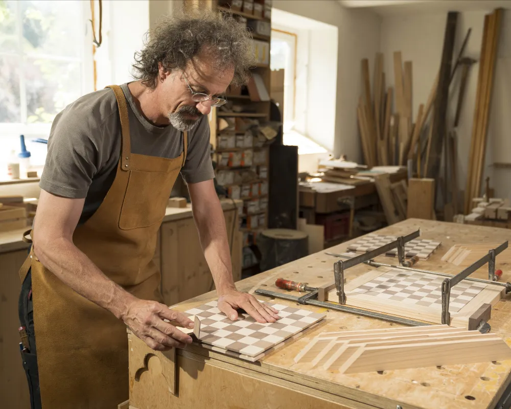 Meister Daschner beim Herstellen eines Schachbretts, in der Werkstatt, beim Schleifen