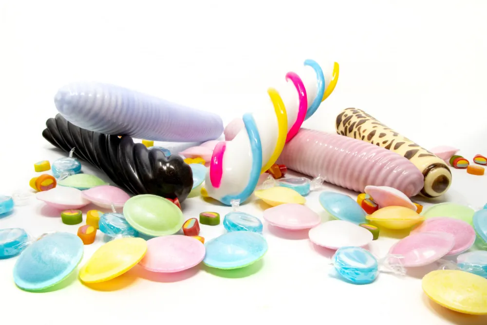 @selfdelve bunte Dildos in Form von Mäusespeck, Lakritzstange und Zuckerwatte liegen zwischen Süßigkeiten