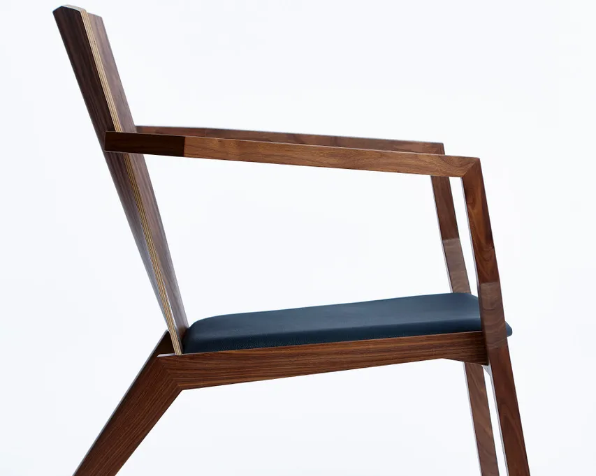 Ein zarter Sessel aus massivem Nussbaumholz mit schwarzem Lederpolster.